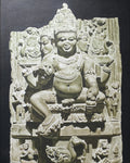 Stone sculpture of a multi-armed deity with intricate carvings on a dark background